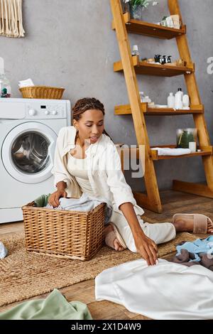 Eine Afroamerikanerin mit Afro-Zöpfen sitzt auf dem Boden neben einem Wäschekorb Stockfoto