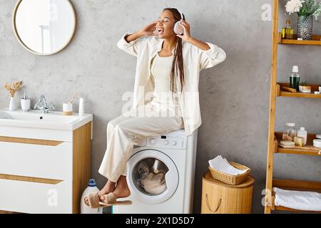 Afroamerikanerin mit Afro-Zöpfen sitzt leise auf einer Waschmaschine und wäscht im Badezimmer. Stockfoto