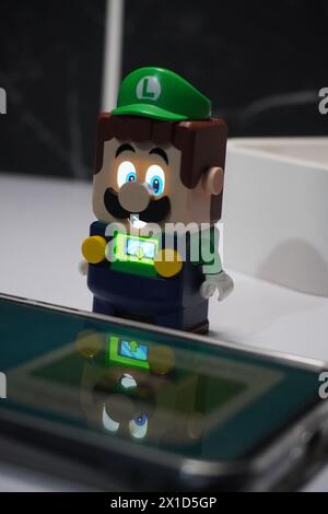 Eine Figur von Luigi aus dem Super Mario Bros-Zeichentrickfilm, die leuchtet und in der Nähe eines beleuchteten Mobiltelefons platziert wird Stockfoto