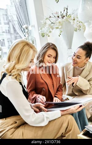 Eine Gruppe junger Frauen, darunter eine wunderschöne Braut, sitzt tief in Gesprächen und Lachen an einem Tisch, während sie eine Hochzeit planen. Stockfoto