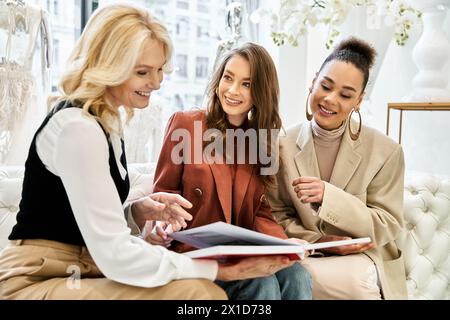 Drei Frauen, darunter eine schöne Braut und ihre besten Freunde, sitzen auf einer Couch, die von einem Brautbuch gefesselt ist. Stockfoto