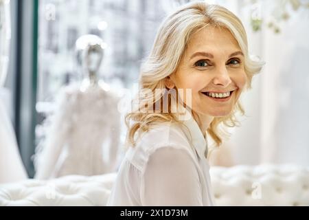 Eine strahlende junge Frau lächelt, während sie vor einer atemberaubenden Ausstellung von Brautkleidern steht, Ladenberater. Stockfoto
