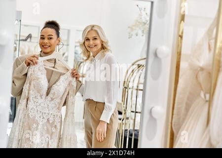 Zwei Frauen, eine junge, schöne Braut und eine Verkäuferin, stehen nebeneinander und bewundern sich im Spiegel. Stockfoto