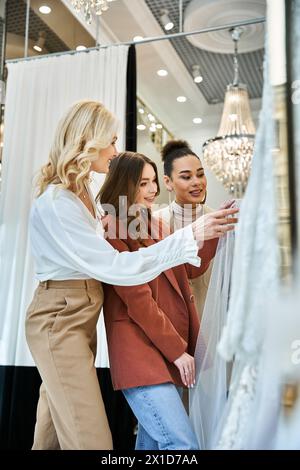 Junge schöne Brautläden für ihr Hochzeitskleid mit ihrer Mutter und der besten Freundin in einem Laden. Stockfoto