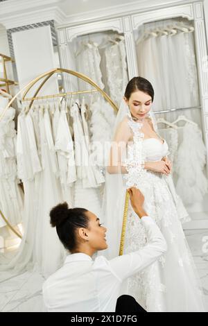 Eine junge brünette Braut in einem Hochzeitskleid wird von einem afroamerikanischen Einkaufsassistenten in einem Brautsalon gemessen. Stockfoto