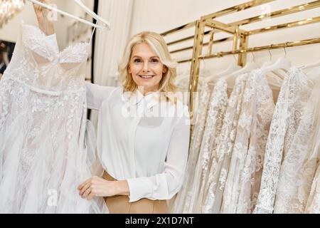 Ein hübscher Einkaufsassistent mittleren Alters steht vor einem Kleiderständer in einem Hochzeitssalon und hilft Kunden. Stockfoto