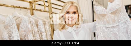 Ein wunderschöner Einkaufsassistent mittleren Alters stöbert in einem Salon in verschiedenen Brautkleidern. Stockfoto