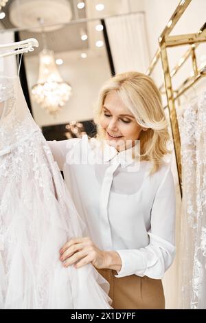 Ein wunderschöner Einkaufsassistent mittleren Alters stöbert in einem Hochzeitssalon in Hochzeitskleidern. Stockfoto