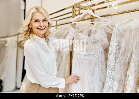 Ein wunderschöner Einkaufsassistent mittleren Alters in einem Hochzeitssalon steht vor einem Kleiderregal und ist bereit, Kunden zu helfen. Stockfoto