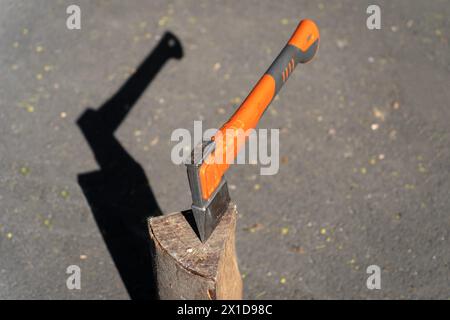 Eine Axt mit einem orangefarbenen Griff, verkeilt in einem Holzblock mit grauem Hintergrund Stockfoto