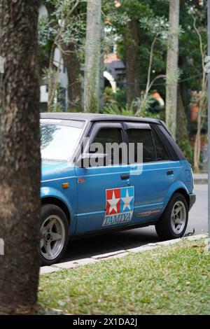 Ein blaues Auto mit einem Tamiya-Aufkleber stand hinter einem Baumstamm im alten Stil Stockfoto