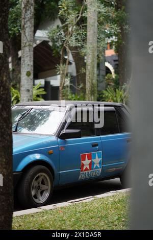 Ein blaues Auto mit einem Tamiya-Aufkleber stand hinter einem Baumstamm im alten Stil Stockfoto