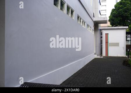 Der Weg neben einem minimalistischen Gebäude führt zu einem kleinen Raum mit bunten Rohren und einem Baum dahinter Stockfoto