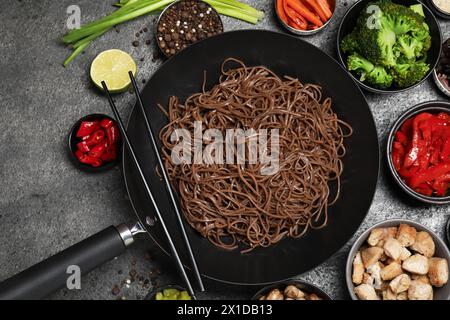 Wok mit Nudeln, Huhn und anderen Produkten auf grauem Tisch, flach gelegt Stockfoto