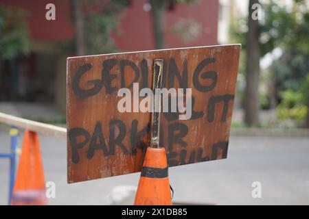 Ein Schild mit der Aufschrift „gedung elit Parkir sulit“ auf Indonesisch, was bedeutet, dass es ein Elite-Gebäude hat, aber das Parken ist schwierig, ist am Straßenkegel angebracht Stockfoto