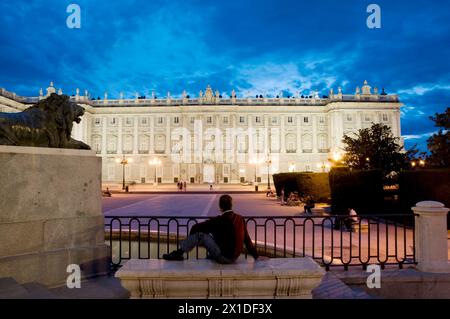 Mann, der auf der Bank sitzt und auf den Königspalast blickt, Nachtsicht. Oriente Square, Madrid, Spanien. Stockfoto