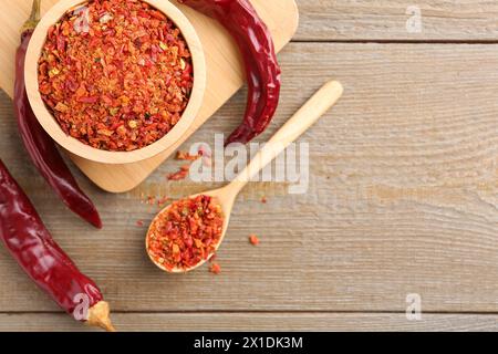 Aromatisches Gewürz. Rote Chilischoten in Schüssel, Löffel und Schoten auf Holztisch, flach gelegt. Leerzeichen für Text Stockfoto