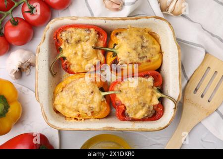 Köstliche gefüllte Paprika in Backform, Spachtel und Zutaten auf weißem, strukturiertem Tisch, flach gelegt Stockfoto