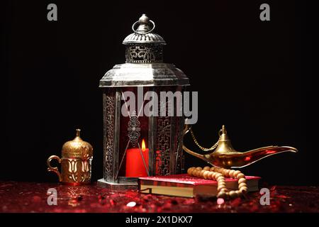 Arabische Laterne, Koran, misbaha und Aladdin magische Lampe auf glänzend rotem Tisch Stockfoto