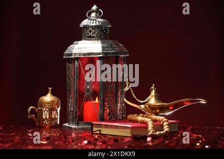 Arabische Laterne, Koran, misbaha und Aladdin magische Lampe auf glänzend rotem Tisch Stockfoto