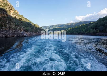 Wasser mit Schaum aufgrund der Turbinen eines Bootes mit Bergen und blauem Himmel im Hintergrund an der ribeira sacra in Lugo, Spanien Stockfoto