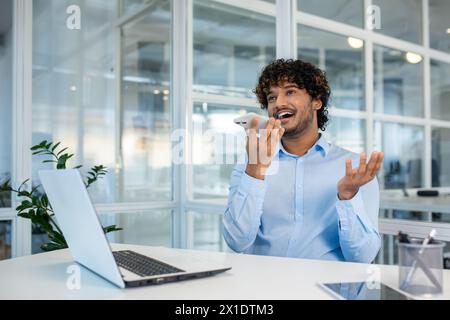 Fröhlicher junger männlicher Profi, der eine unbeschwerte Unterhaltung auf seinem Smartphone in einer hellen und modernen Büroumgebung genießt. Stockfoto