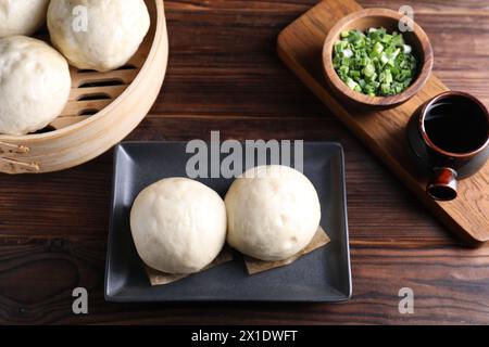 Köstliche chinesische gedämpfte Brötchen, grüne Zwiebeln und Sojasauce auf Holztisch, flache Ladefläche Stockfoto