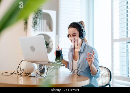 Frau mit Kopfhörern, die an einem Schreibtisch sitzt und in ein Mikrofon spricht und einen Podcast aufnimmt Stockfoto