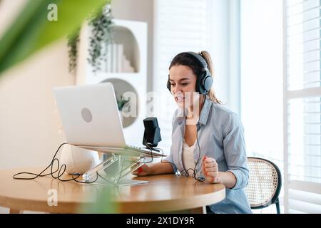 Frau mit Kopfhörern, die an einem Schreibtisch sitzt und in ein Mikrofon spricht und einen Podcast aufnimmt Stockfoto