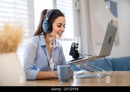 Frau mit Kopfhörern, die an einem Schreibtisch sitzt und in ein Mikrofon spricht und einen Podcast aufnimmt Stockfoto