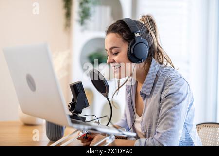 Frau mit Kopfhörern, die an einem Schreibtisch sitzt und in ein Mikrofon spricht und einen Podcast aufnimmt Stockfoto