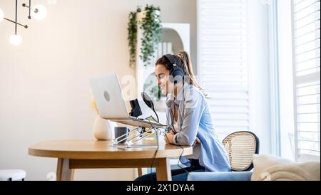 Frau mit Kopfhörern, die an einem Schreibtisch sitzt und in ein Mikrofon spricht und einen Podcast aufnimmt Stockfoto