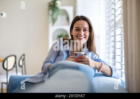 Lächelnde Frau mit Mobiltelefon auf dem Sofa im Wohnzimmer Zu Hause Stockfoto