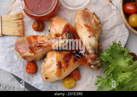 Marinade, Bratenbürste, gebratene Hähnchenstangen, Tomaten und Salat auf dem Tisch, flache Lay Stockfoto