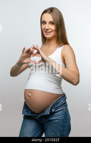 Schwangere junge Frau mit Herzzeichen und einem schönen Lächeln Stockfoto