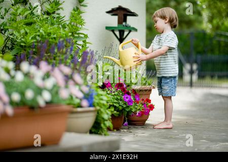 Süßer kleiner Junge, der am Sommertag im Hinterhof Blumenbeete tränkt. Kind mit Gießkanne zum Gießen von Pflanzen. Kind hilft bei den alltäglichen Aufgaben. Mommy Stockfoto