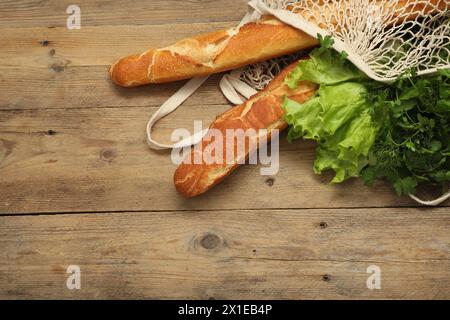 Schnur-Tasche mit frischen Baguettes, Salat und Kräutern auf hölzernem Hintergrund, Draufsicht. Leerzeichen für Text Stockfoto