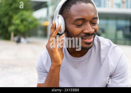 Musiksong-Konzept. Guter Start in den Tag. Glücklicher Afroamerikaner, der moderne Hit auf der Straße in der Stadt hört. Person Guy mit Kopfhörern genießen Sie Ihre Lieblingsmusik im Freien. Lebensfreude der Menschen Stockfoto