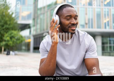 Musiksong-Konzept. Guter Start in den Tag. Glücklicher Afroamerikaner, der moderne Hit auf der Straße in der Stadt hört. Person Guy mit Kopfhörern genießen Sie Ihre Lieblingsmusik im Freien. Lebensfreude der Menschen Stockfoto