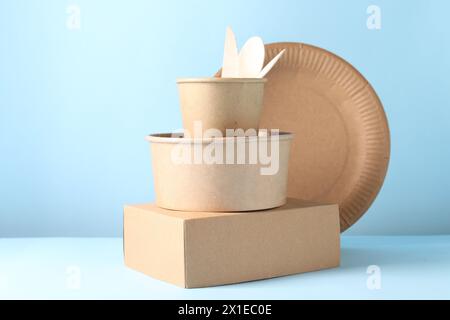 Umweltfreundliche Lebensmittelverpackungen. Papierbehälter und Geschirr auf weißem Tisch vor hellblauem Hintergrund Stockfoto
