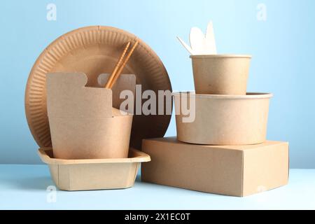 Umweltfreundliche Lebensmittelverpackungen. Papierbehälter und Geschirr auf weißem Tisch vor hellblauem Hintergrund Stockfoto