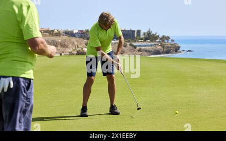 Golfer auf dem Grün mit einem Putter in der Hand. Der Spieler auf dem Grün schlägt den Ball in Richtung Loch. Stockfoto