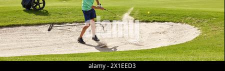 Der Golfspieler schlägt den Ball aus dem Bunker mit einem Golfschläger an einem sonnigen Sommertag. Stockfoto