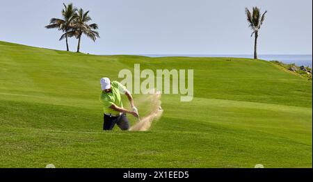 Der Golfspieler schlägt den Ball aus dem Bunker mit einem Golfschläger an einem sonnigen Sommertag. Stockfoto