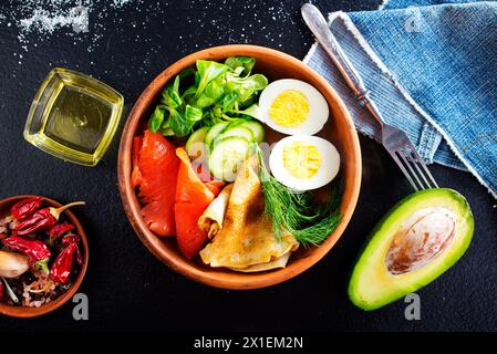 Köstlicher gesunder Brunch - gekochtes Ei, geräucherter Lachs, grüner Salat und herzhafte Pfannkuchen auf dunklem Hintergrund Stockfoto