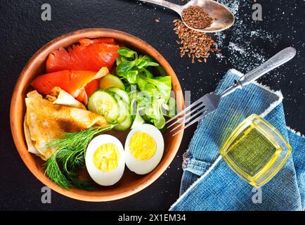 Köstlicher gesunder Brunch - gekochtes Ei, geräucherter Lachs, grüner Salat und herzhafte Pfannkuchen auf dunklem Hintergrund Stockfoto