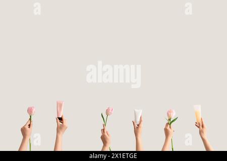 Frauen mit Tuben aus Handcreme und Tulpen auf hellem Hintergrund Stockfoto
