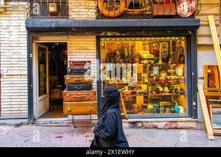 Eine Dame in einer Burka läuft an einem Antiquitätenladen in Istanbul vorbei, mit hoch gestapelten Vintage-Koffern und Kuriositäten im Schaufenster. Stockfoto