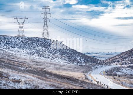 Elektrische Pylonen auf einem Hügel mit Stromleitungen über einem Tal mit Blick auf die gewundene Straße in Alberta Kanada. Stockfoto