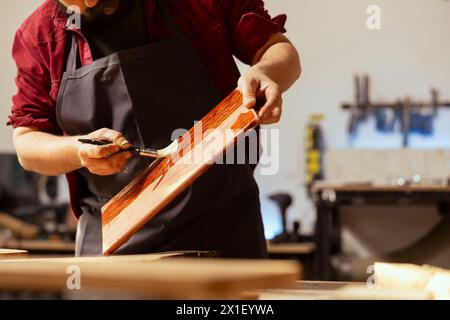 Zimmermann trägt Wachs auf Holzoberfläche auf, um Beschädigungen zu vermeiden und eine Schutzschicht zu bieten. Holzbearbeitungsexperte in der Montagewerkstatt, die Holzdielen veredelt und Ölschichten aufträgt Stockfoto